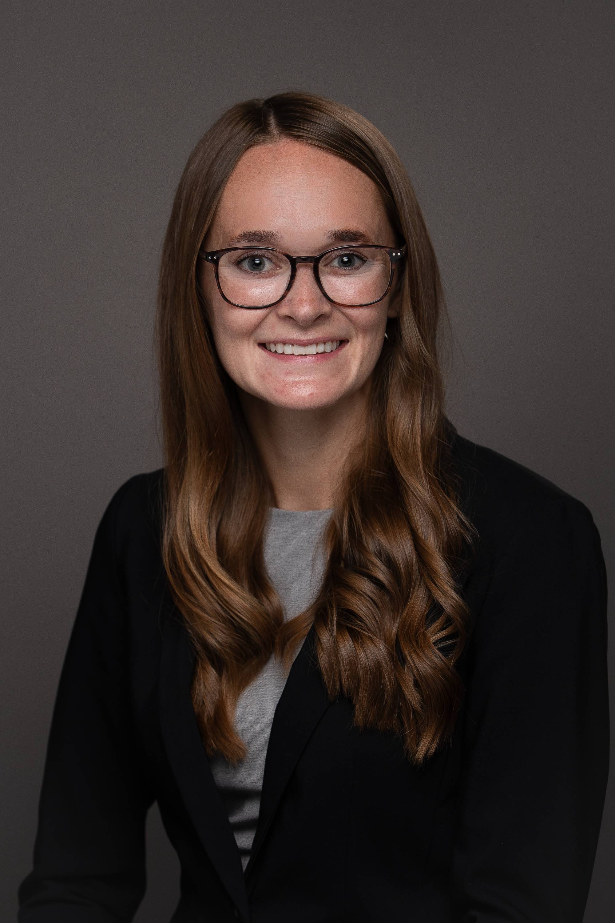 Emily Zeliasko portrait photo with a black blazer and gray shirt on with glasses.